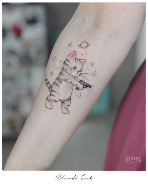 Minimalistyczny tatuaż na przedramieniu przedstawiający kota z pistoletem